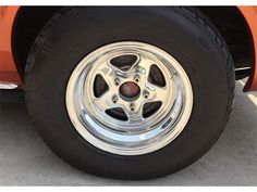 an orange car with chrome spokes parked in a parking lot