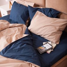 an unmade bed with blue and tan sheets, pillows and a book on it