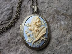 "Beautiful cameo locket, choose bronze, antiqued silver, or silver (other colors and styles are available in my shop so please do browse The cameo is a gorgeous lily of the valley. Stunning colors. cream on sky blue. The bronze and silver plated lockets are Victorian style with beautiful scroll on both the front and back about 2\" long, please see the photos. They can hold two photos, a treasured keepsake or both. Pass down from generation to generation The bronze locket includes a 24\" adjustab Nickel-free Brass Locket Necklace For Wedding, Handmade Antique Gold Jewelry For Keepsake, Antique Finish Pendant Jewelry For Wedding, Wedding Engraved Bronze Locket Necklace, Antique Gold Engraved Locket Necklace For Wedding, Heirloom Antique Finish Necklace For Weddings, Silver Brass Locket Necklace For Weddings, Heirloom Wedding Necklace With Antique Finish, Heirloom Antique Finish Wedding Necklace