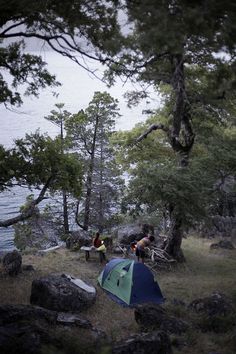 two people are camping in the woods by the water