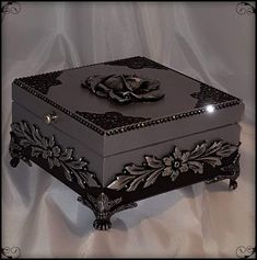 an ornate black box with flowers and jewels on the lid is sitting on a white sheet