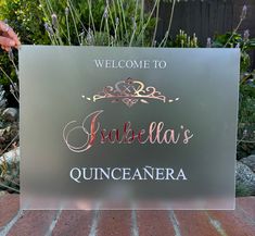 a welcome sign is displayed in front of some plants and flowers on a brick surface