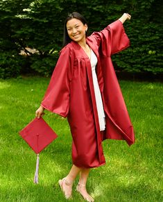 a woman in a red graduation gown and cap with her arms out, smiling at the camera