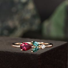 two rings with different colored stones sitting on top of a black box next to a green plant