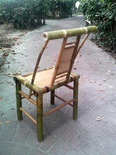 a chair made out of bamboo sitting on a sidewalk in front of some bushes and trees