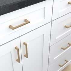 a white kitchen with black counter tops and gold pulls on the drawers in front of it