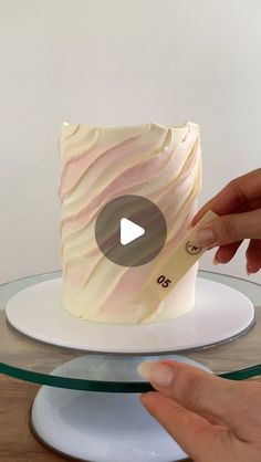 someone is decorating a cake with white frosting and pink icing on it