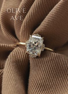 an engagement ring on top of a brown cloth with the words olive ave written above it