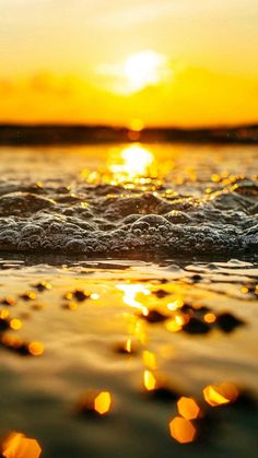 the sun is setting over the ocean with small bubbles in the water on the beach