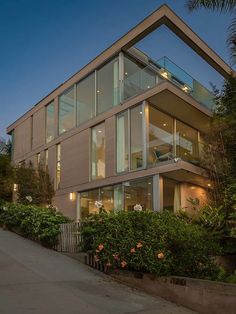 a modern house with large windows and lots of greenery on the side of it