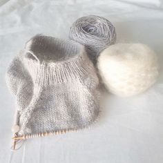 two balls of yarn sit next to a knitted mitt on a white sheet