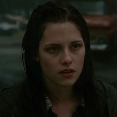 a woman with dark hair and black eyes stares at the camera while standing in front of a car