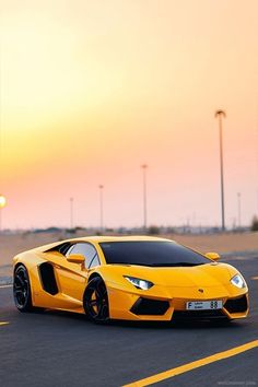 a yellow sports car is driving down the road at sunset or dawn in an empty parking lot