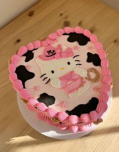 a hello kitty birthday cake with pink and black icing on a wooden table top