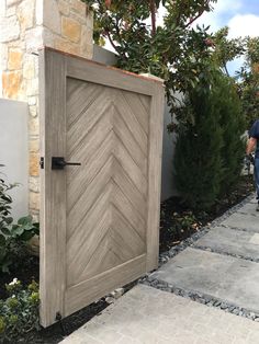 a man walking past a wooden door on a sidewalk next to a stone wall and shrubbery