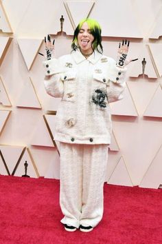 a woman with green hair standing on a red carpet in front of an oscars backdrop