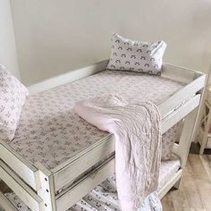 a white wooden bunk bed sitting next to a small table with pillows on top of it