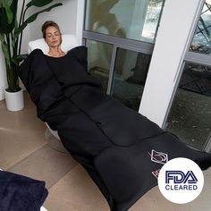 a woman sitting in a white chair with a black blanket over her face and on the floor next to a plant