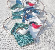 four ceramic bird ornaments sitting on top of a white cloth covered table with beads and thread