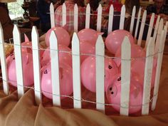 pink piggy bank sitting in front of a white picket fence with balloons attached to it