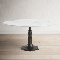 a white marble top dining table with black pedestals on wooden floors in an empty room