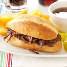 a roast beef sandwich on a plate with fries and pickles next to dipping sauce