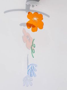 an orange flower is hanging from a metal hook on a white wall with shadow and light