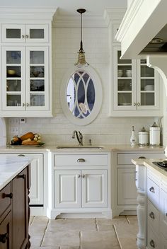 a kitchen with white cabinets and an oval mirror on the wall above the stove top