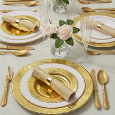 the table is set with gold and white plates, silverware, and flowers in vases