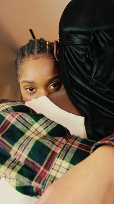 a woman is hugging another woman in a plaid shirt and black head scarf, both looking at the camera