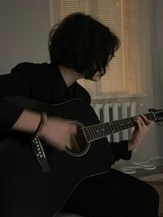 a man sitting on the floor playing a guitar in front of a radiator