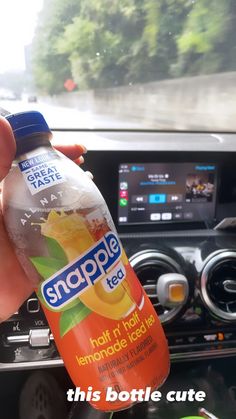 someone is holding a bottle of snapple tea in their hand while driving the car