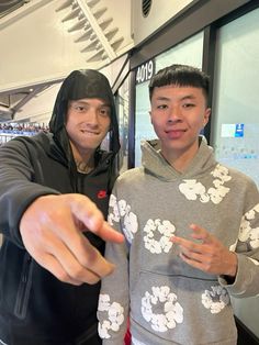 two young men standing next to each other in front of a window and pointing at the camera