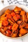 a white bowl filled with cooked carrots on top of a marble counter next to a black and white towel