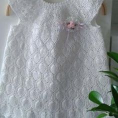 a white crocheted dress hanging on a clothes line with a plant in the corner