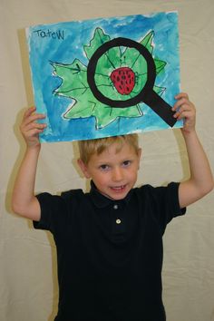 a young boy holding up a drawing with a magnifying glass on top of his head