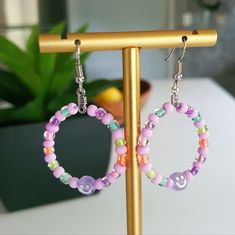 two pairs of colorful beaded hoop earrings on a gold stand next to a potted plant