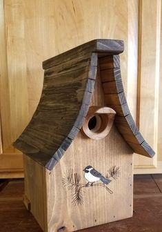 a bird house made out of wood with a bird on it's roof and a birdhouse in the background