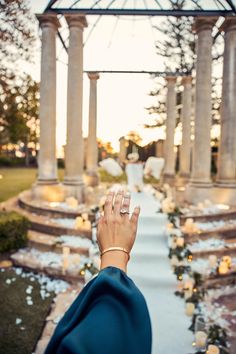 a woman's hand with two wedding rings on her finger in front of an outdoor gazebo