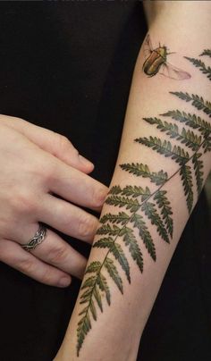 a woman's arm with a green leaf and insect tattoo on the left arm