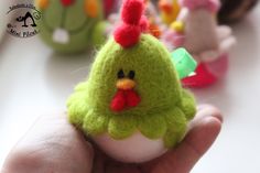 a hand is holding a small green and red toy chicken in it's left hand