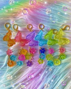 six different colored butterfly charms sitting on top of a white feathered surface with bubbles