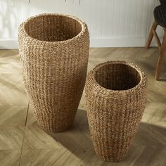 two wicker vases sitting on the floor in front of a potted plant