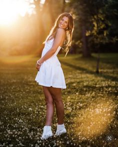 a beautiful young woman posing for a photo in the grass with sun shining behind her