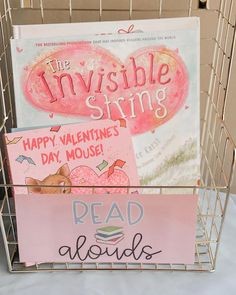 two books in a metal basket on a table next to a sign that says, the invisible string happy valentine's day mouse