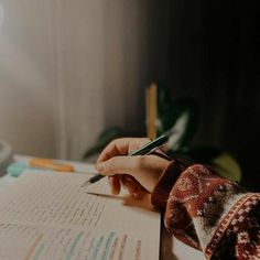 a person writing on a piece of paper with a pen in their left hand and a cup next to it