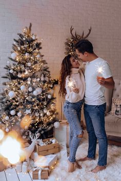 a man and woman standing in front of a christmas tree with presents under the lights