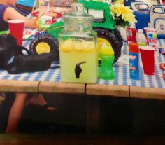 children are sitting at a table with plastic toys and drinks on it, including a tractor