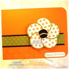 an orange card with a white flower on the front and green ribbon around the bottom