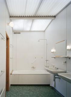 a white bathroom with green tile flooring and a bathtub in the corner next to a sink